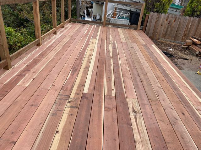 Unfinished wooden deck boards installed on a raised outdoor platform beside a yard and fence.