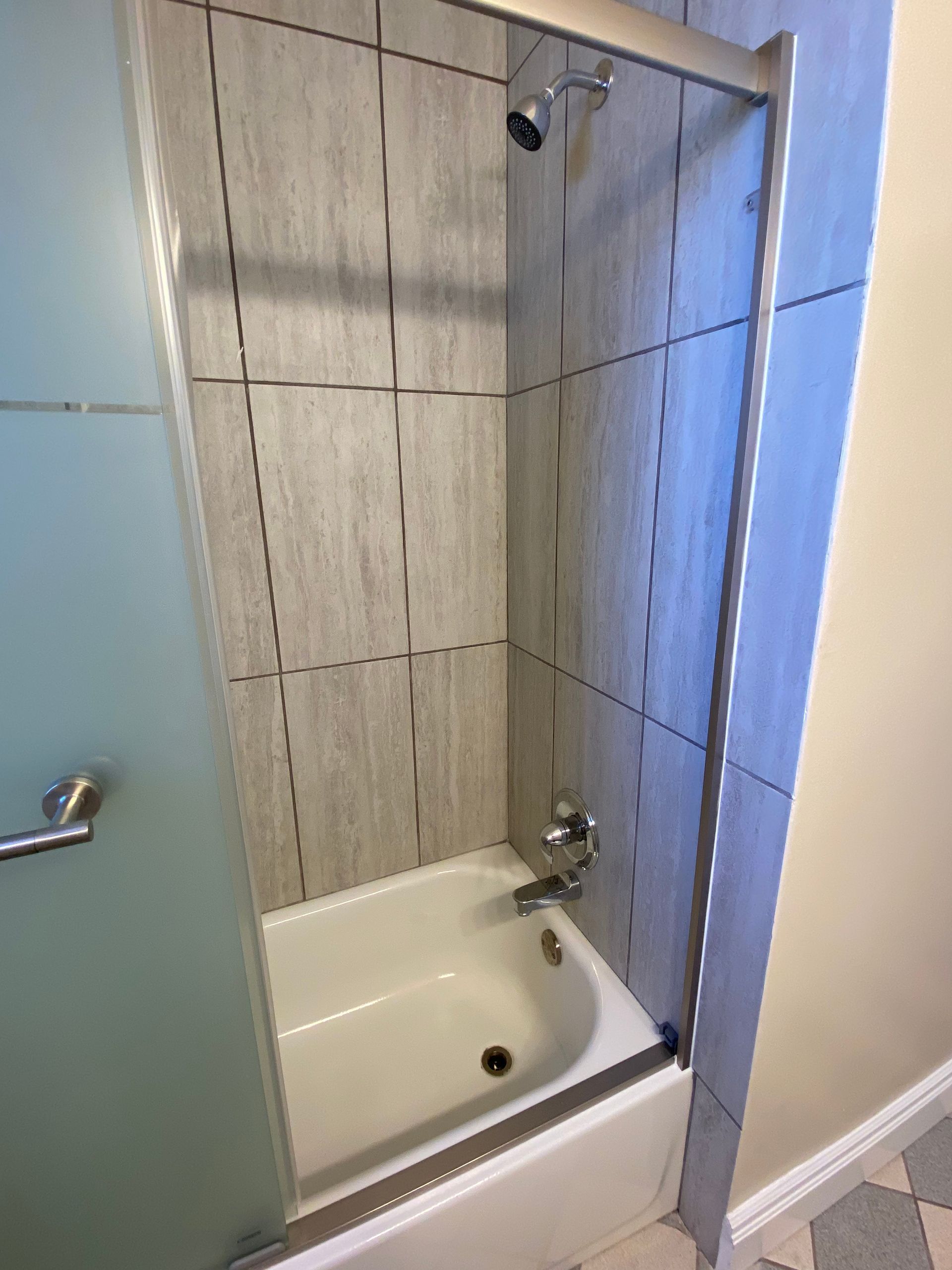 Tiled shower stall with a small bathtub, frosted glass door, and wall-mounted showerhead
