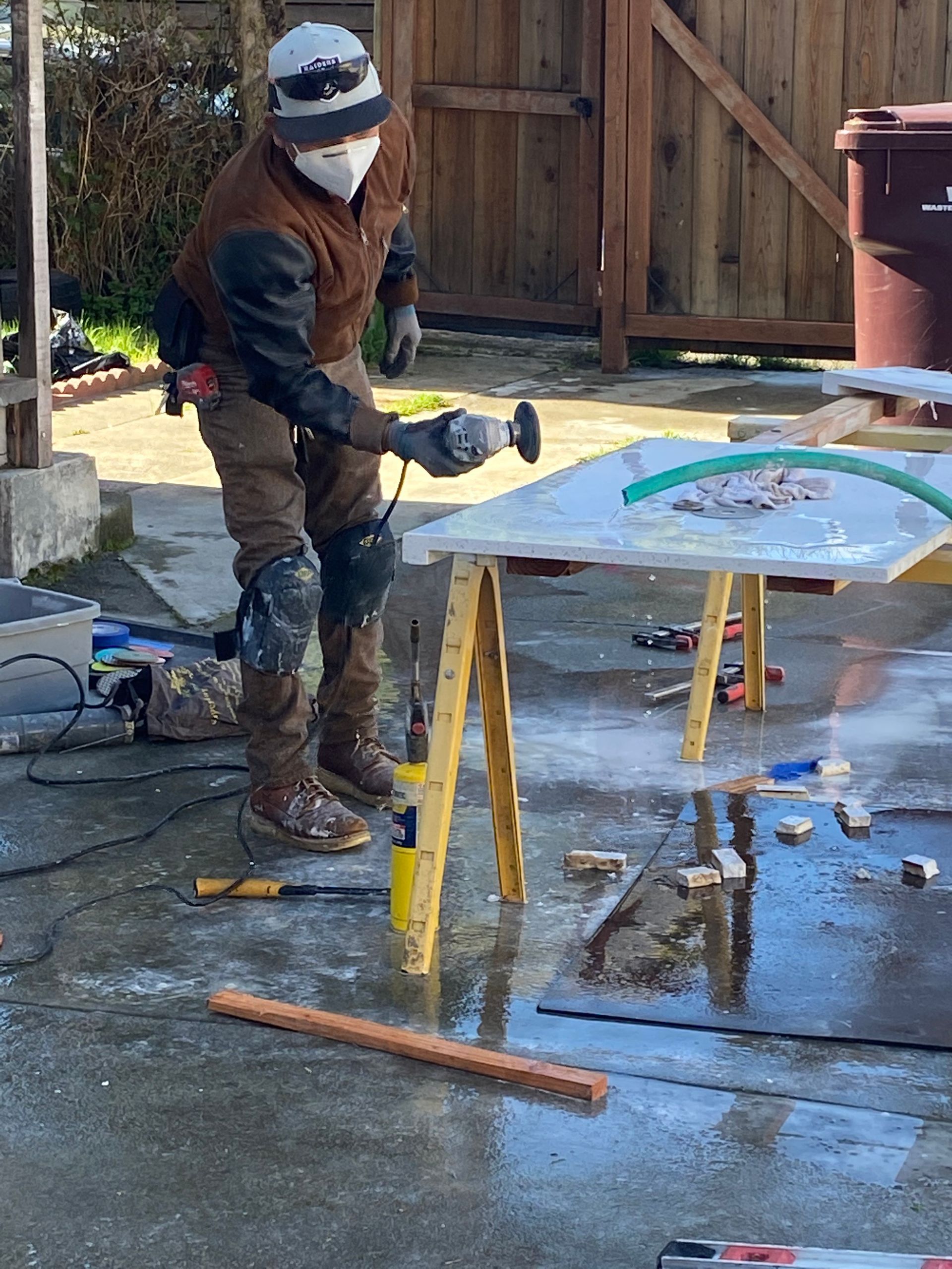 Person sanding a colorful board on sawhorses in a wet outdoor workspace