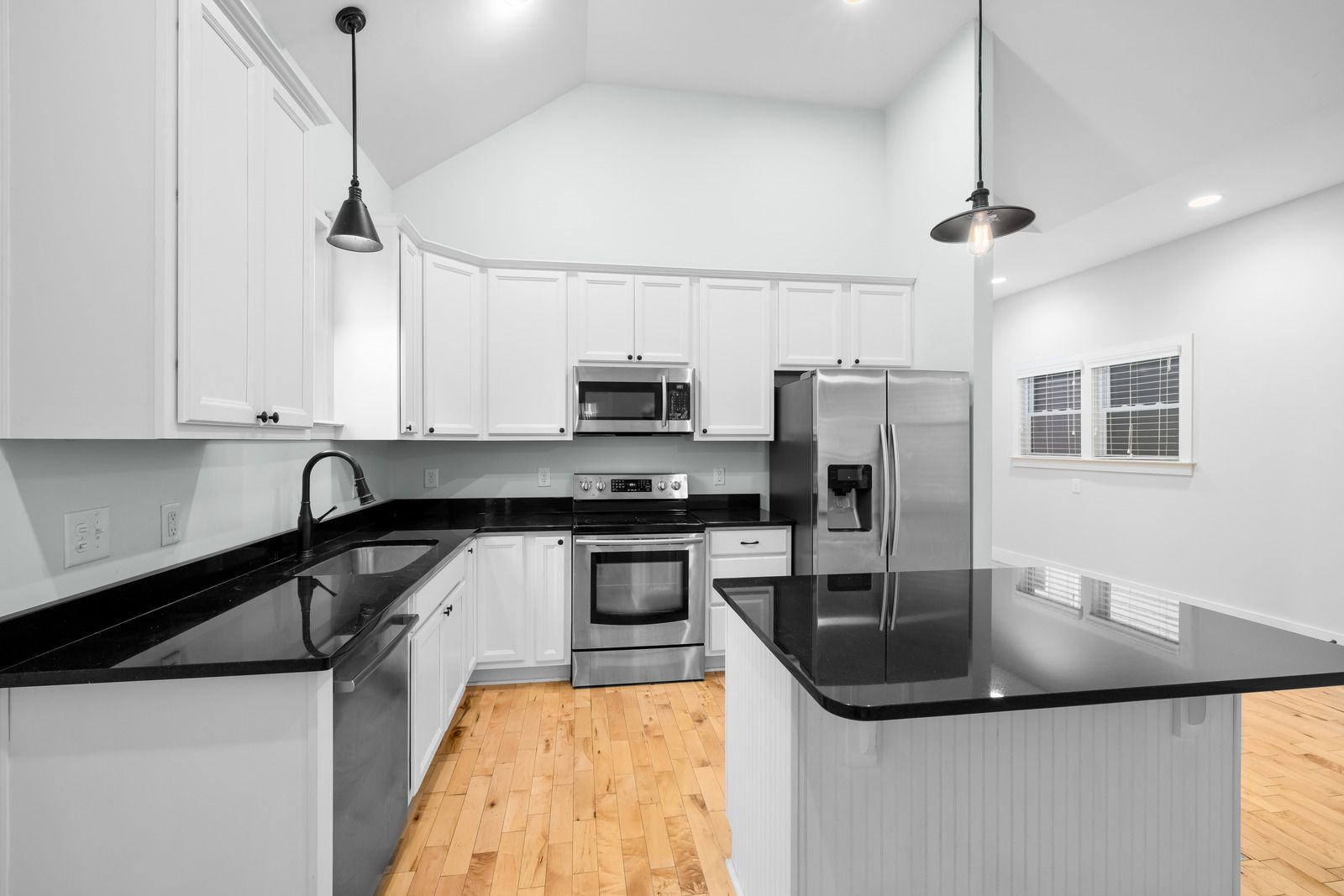 Bright modern kitchen with white cabinets, black countertops, stainless steel appliances, and wood flooring