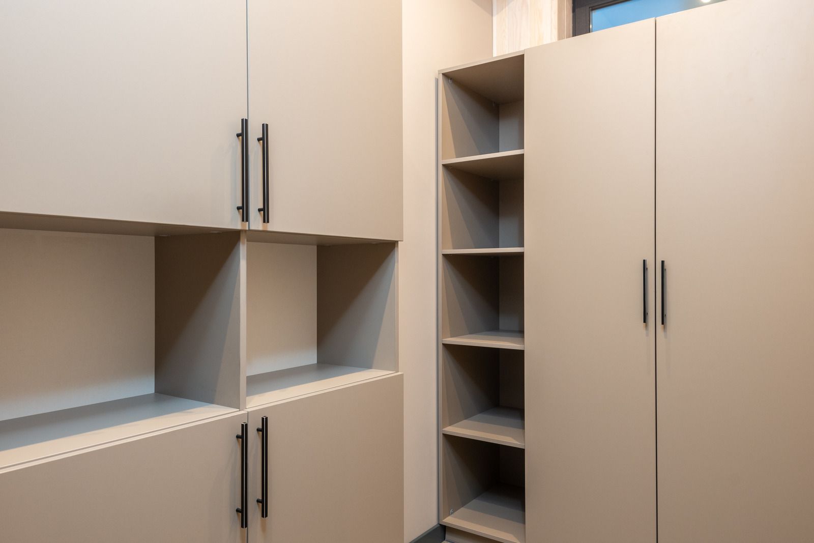 Built-in beige cabinets with open shelves and metal handles in a kitchen or storage area