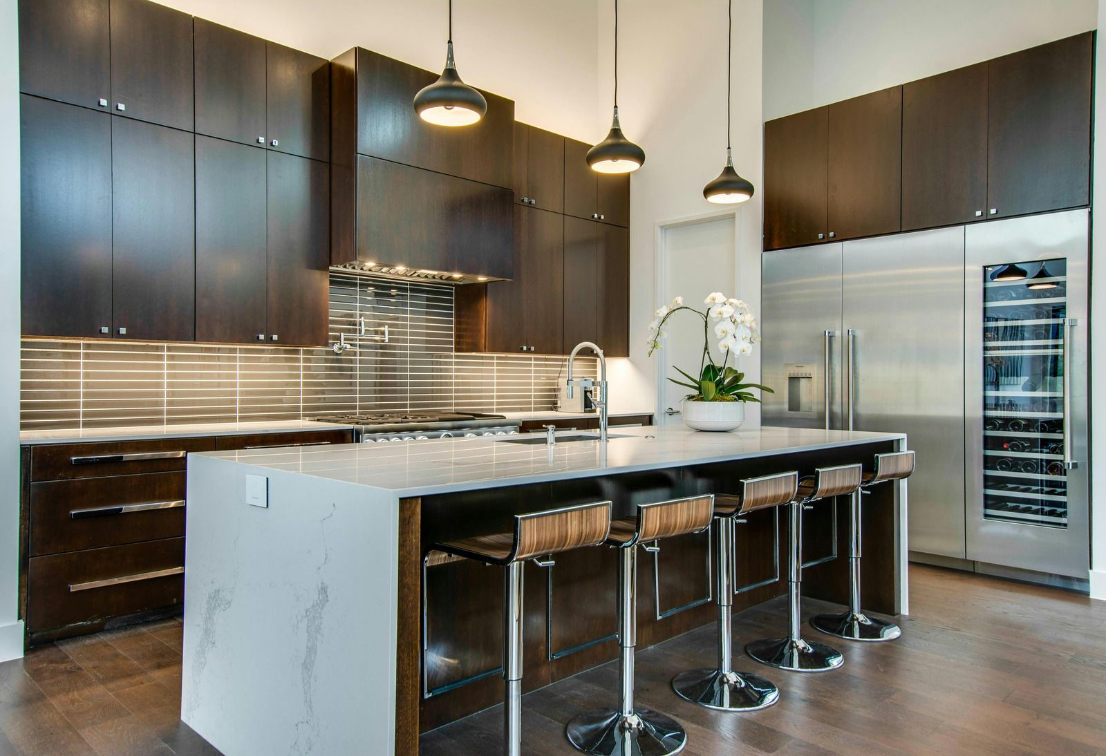 Modern kitchen with dark wood cabinets, white island, pendant lights, and four bar stools