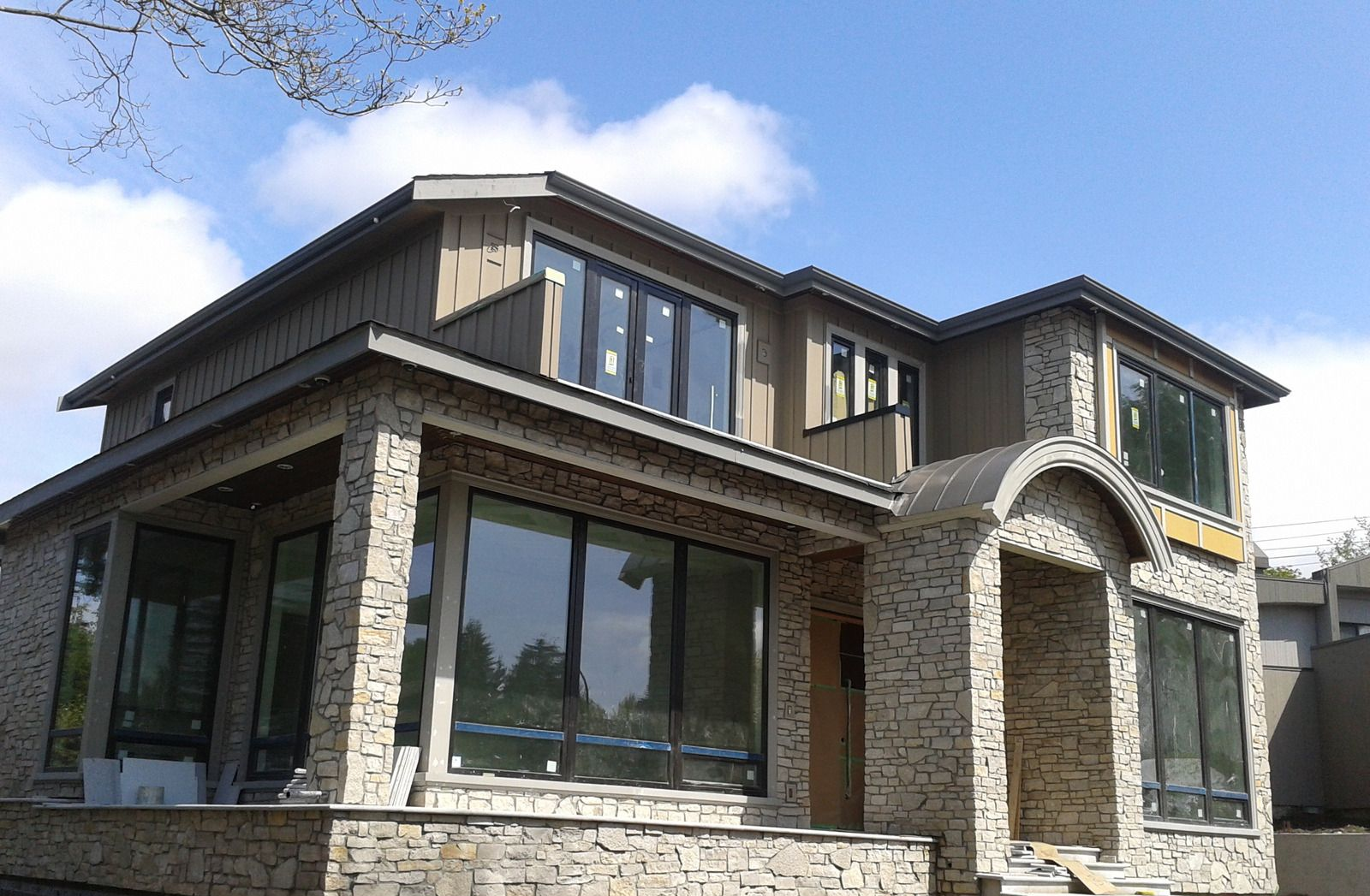 Modern two-story brick house with large windows and a stone entry under a partly cloudy sky