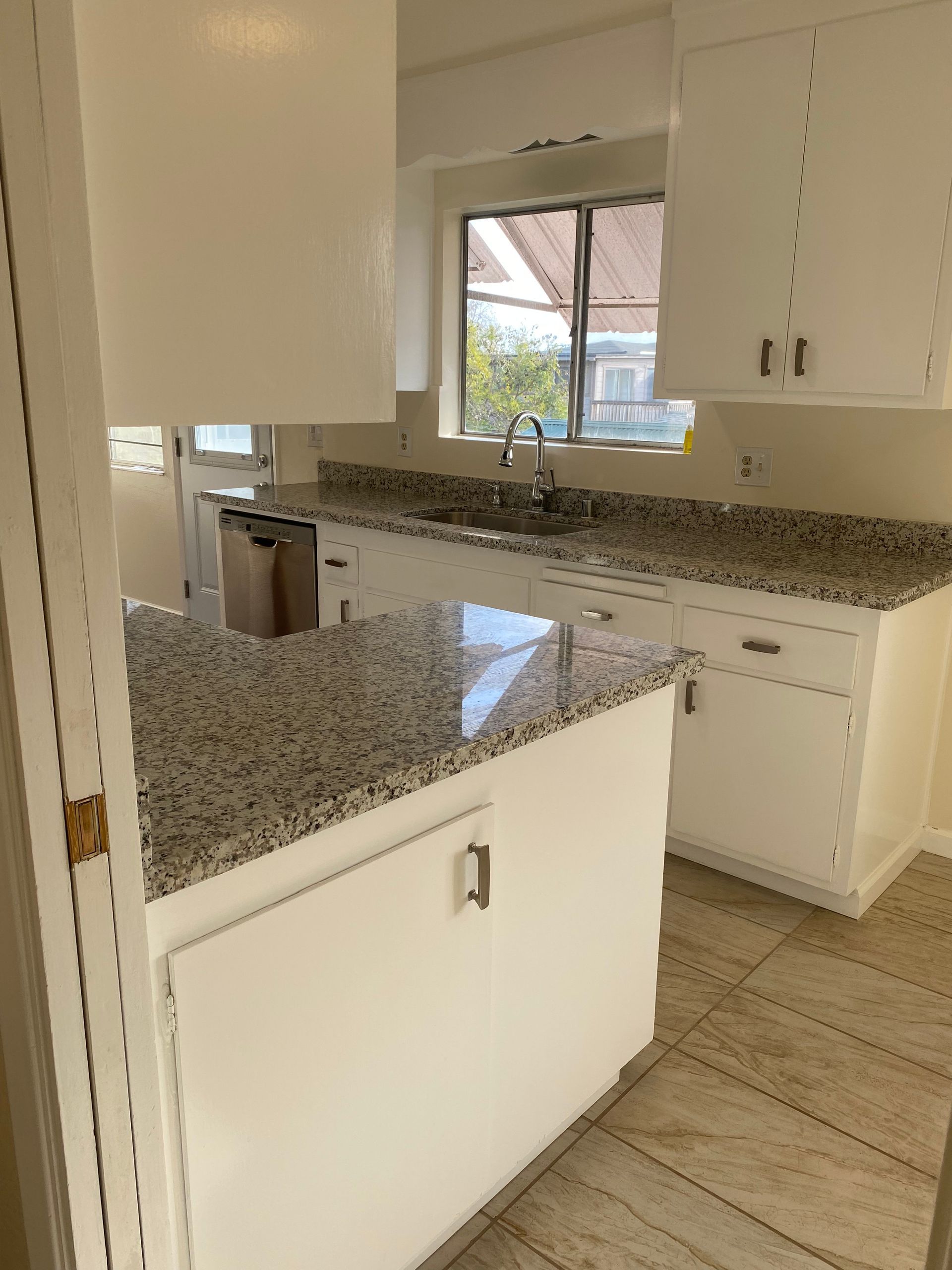 Bright modern kitchen with white cabinets, speckled granite countertops, and a window over the sink.