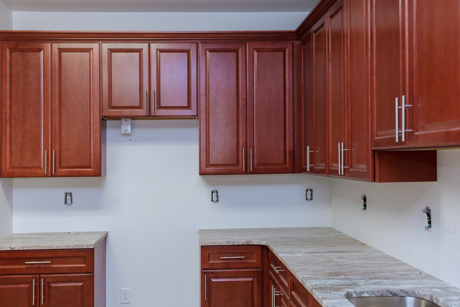 Empty kitchen with cherry wood cabinets and light marble countertops, no appliances installed.