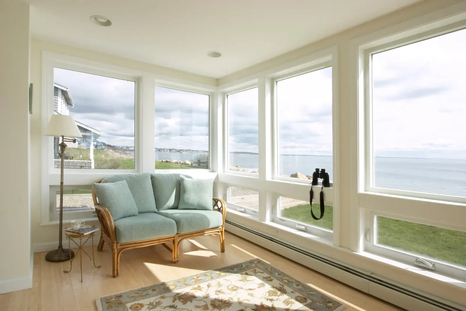 Bright sunroom with large windows, a mint loveseat, floor lamp, and ocean view