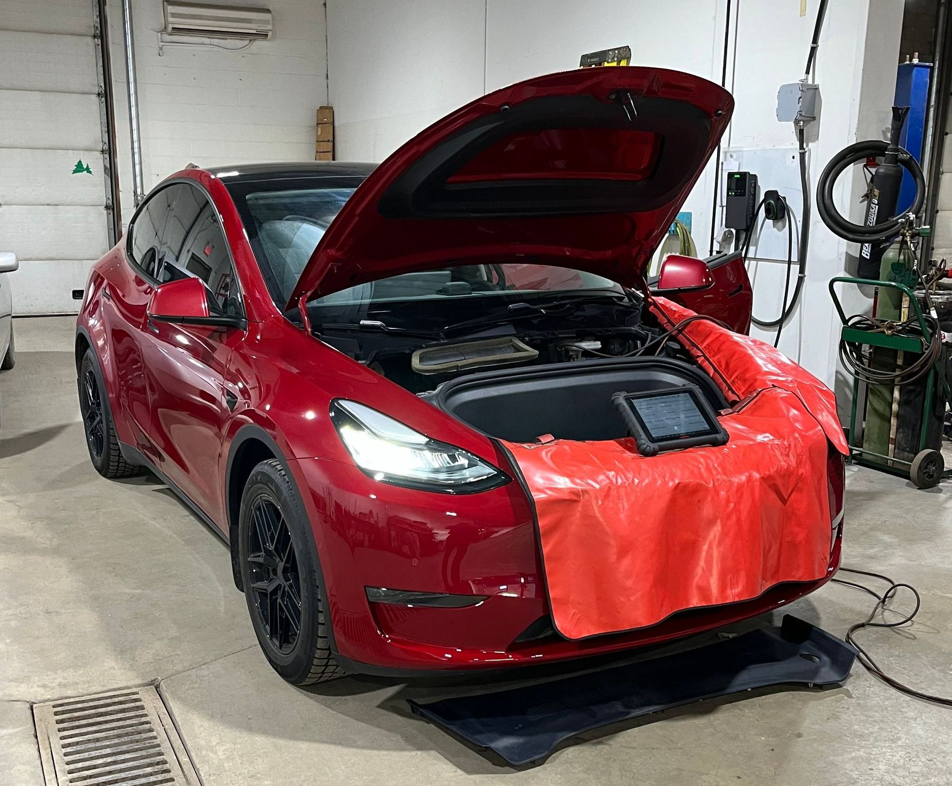 A red tesla model y with its hood open in a garage. - Fleming Automotive
