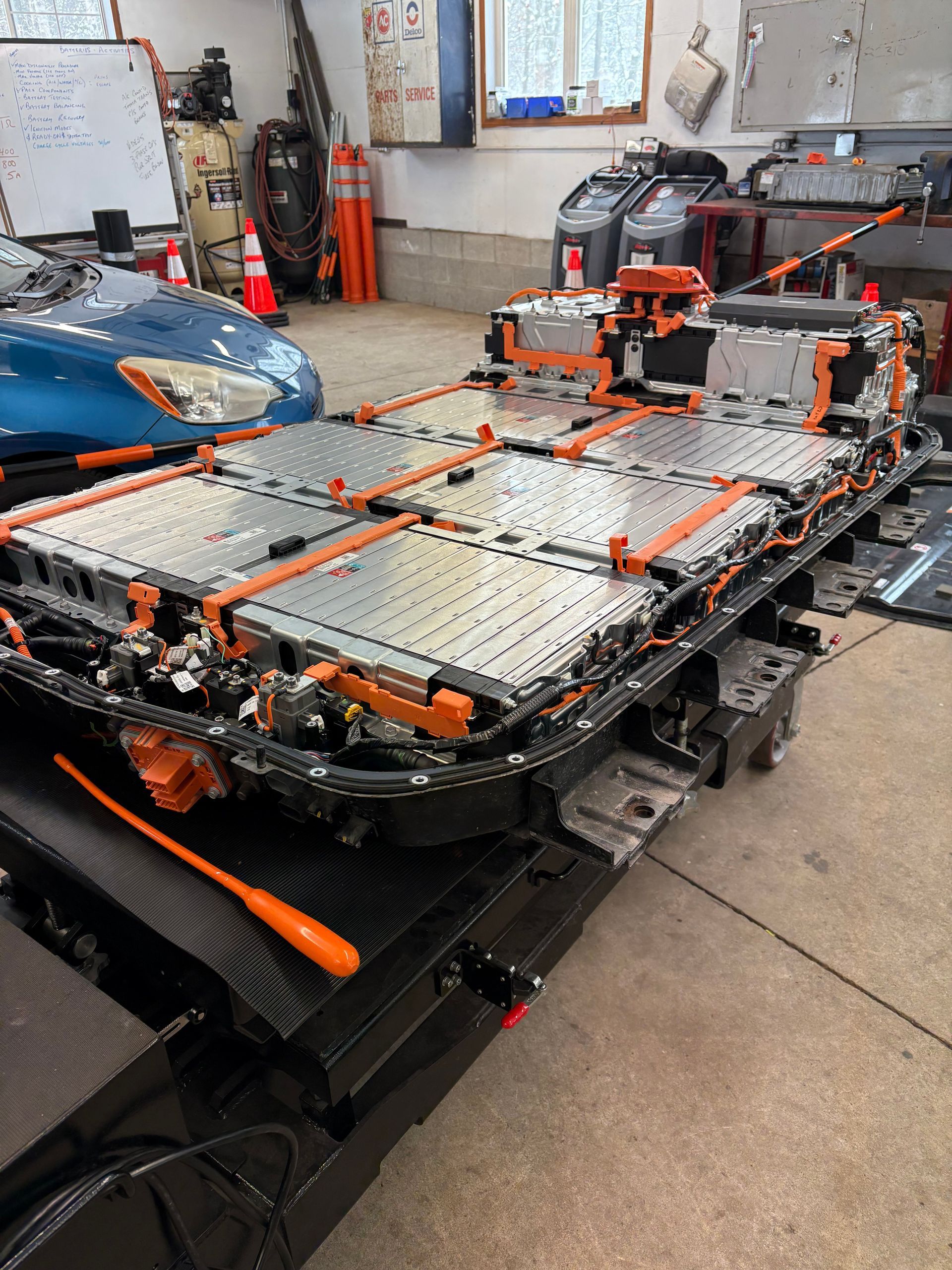 A blue car is sitting in a garage next to a large battery.