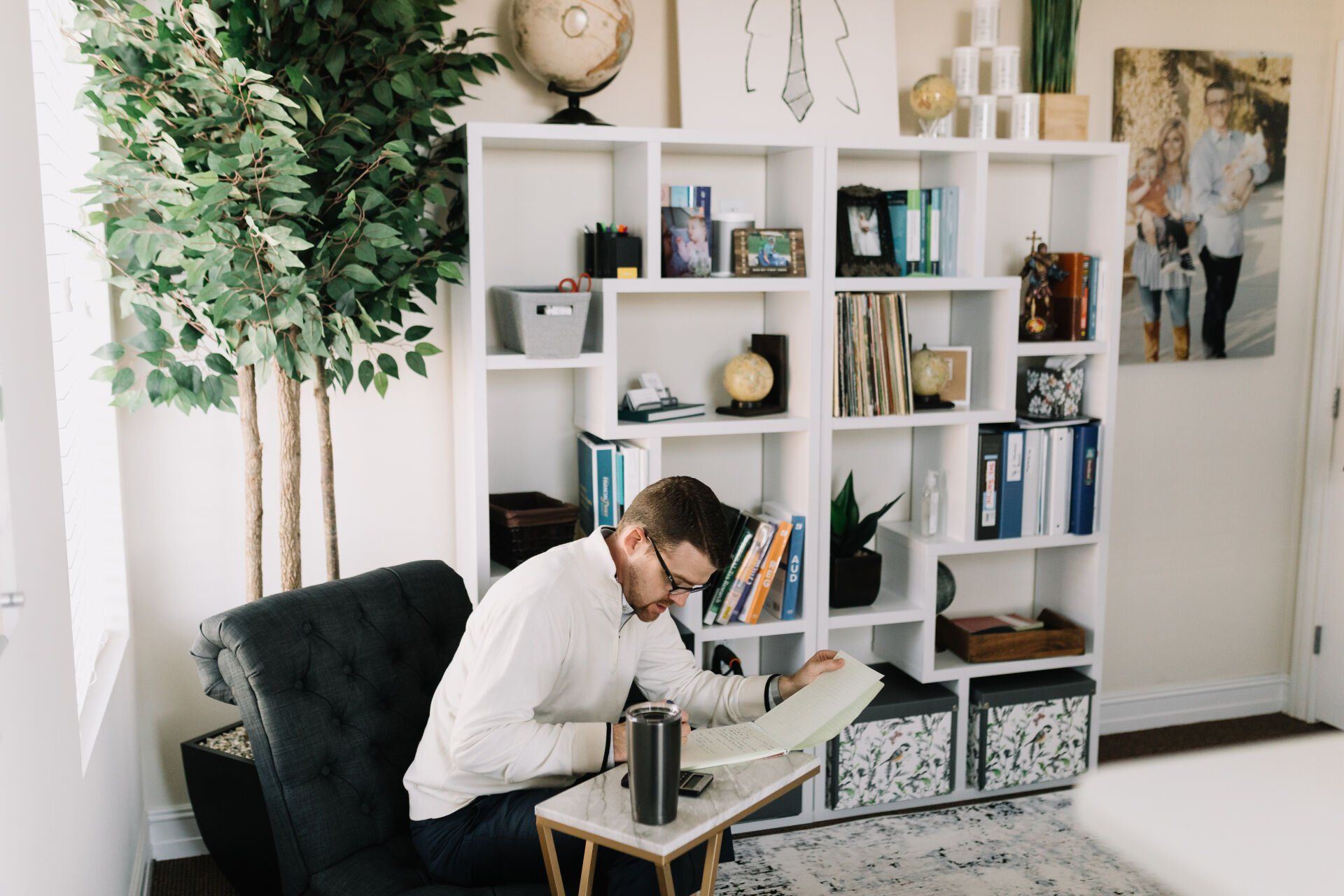 A man is sitting in a chair reading a book in a living room.