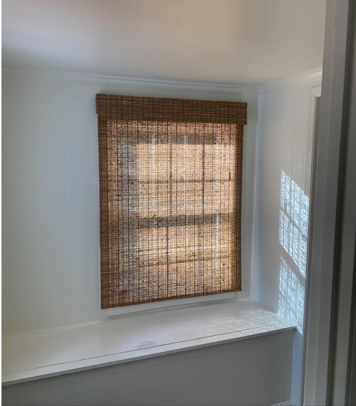 Small white room with a woven brown window shade letting in soft daylight.