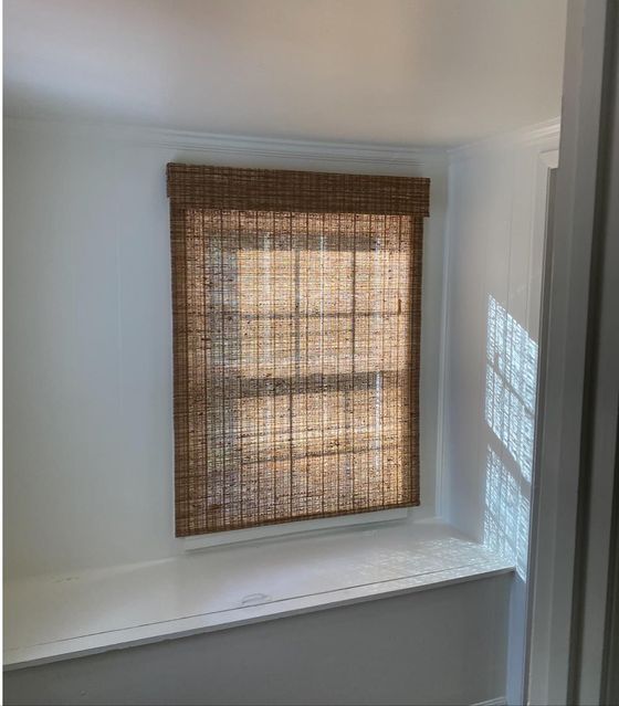 Woven bamboo shade on a small window in a white room, with light casting a pattern on the wall.