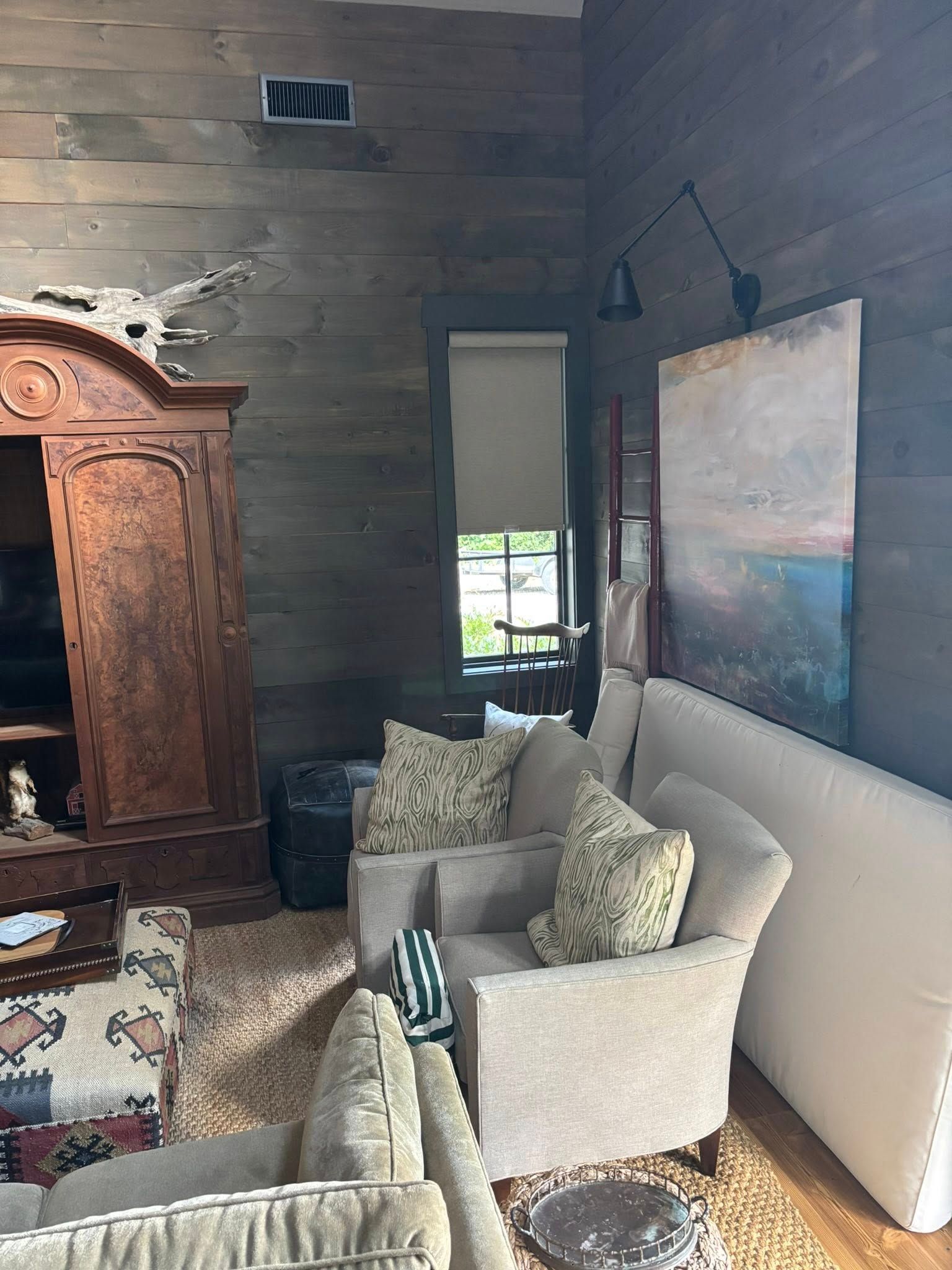 Cozy living room with beige armchairs, a sofa, large wall art, and a wooden cabinet against dark wood walls
