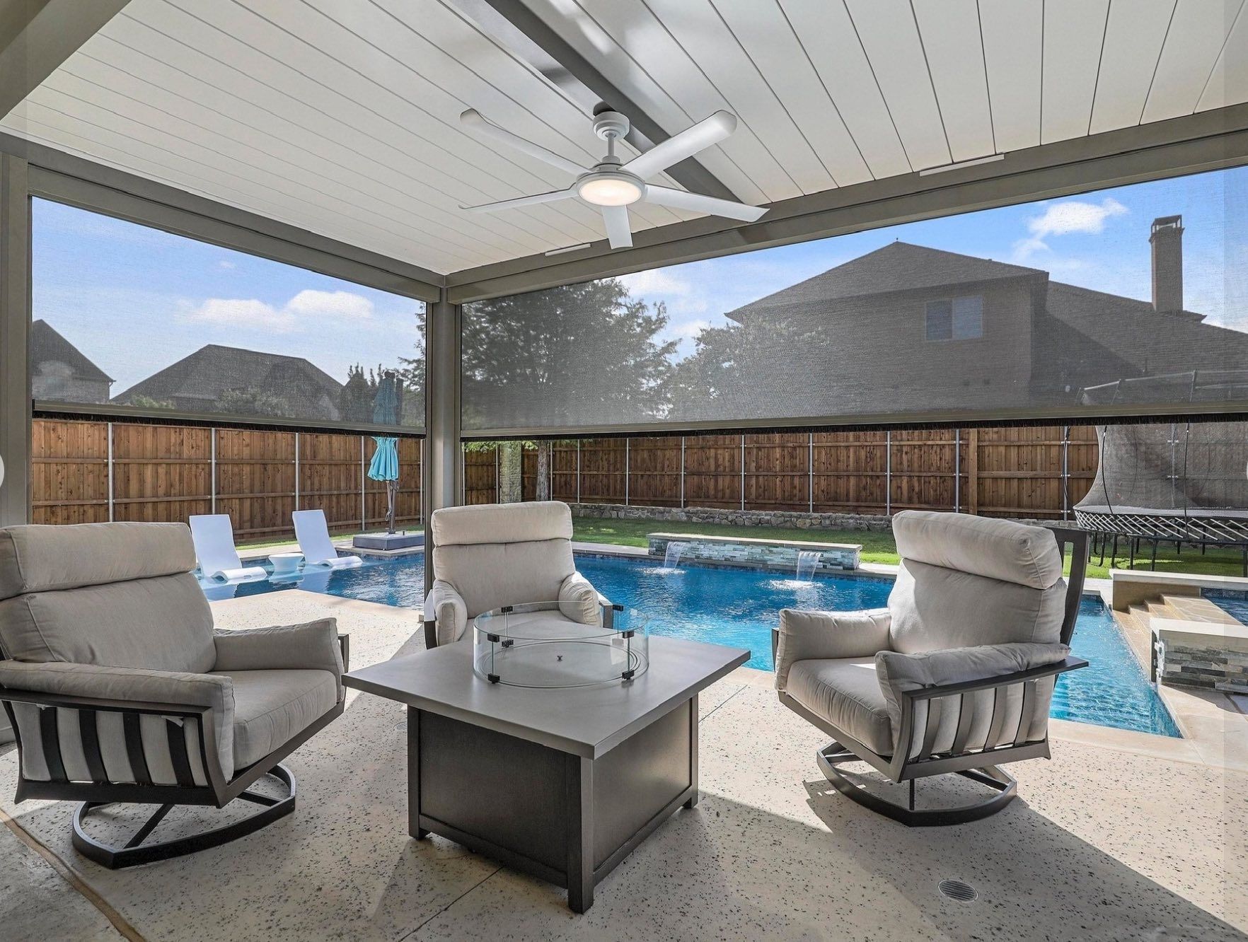 Covered patio with gray seating around a fire table beside a backyard pool.