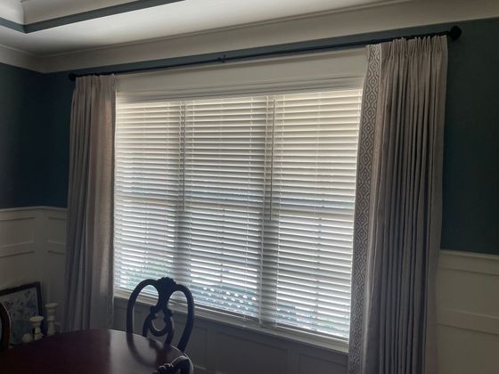 Dining room window with white blinds and curtains, blue walls, and a chair by the table