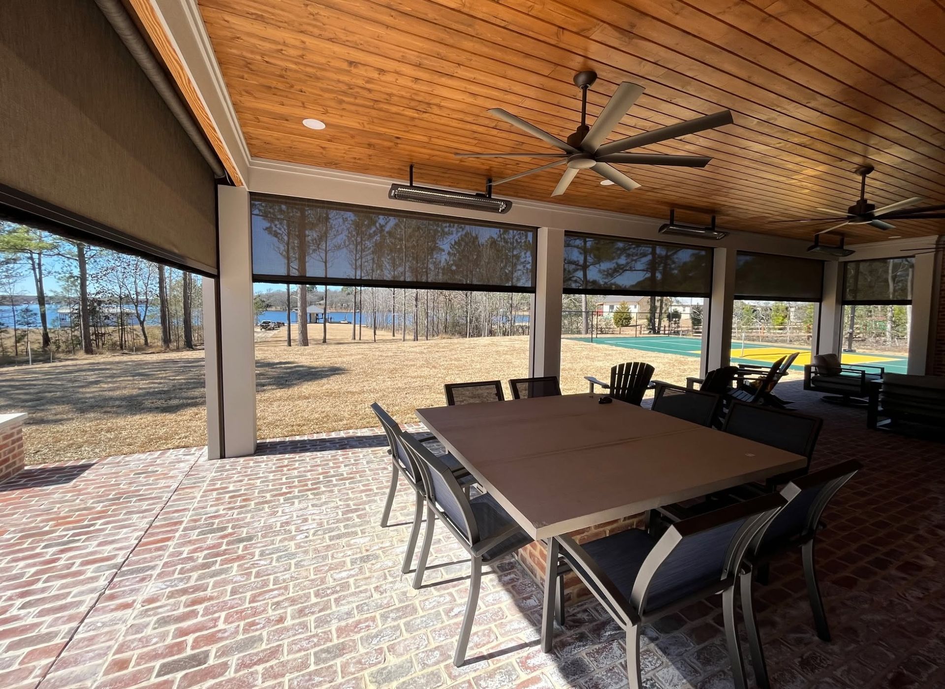 Covered patio with brick floor, wood ceiling, dining table, chairs, and outdoor view through screened openings