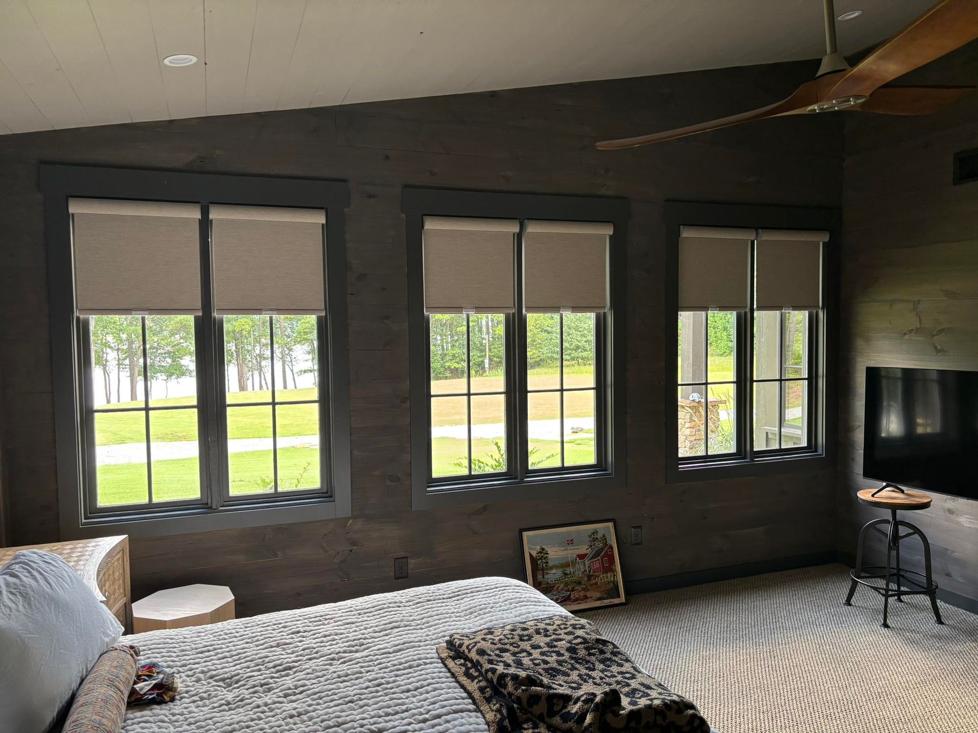 Bedroom with large windows, gray walls, bed, patterned rug, and view of a green yard outside