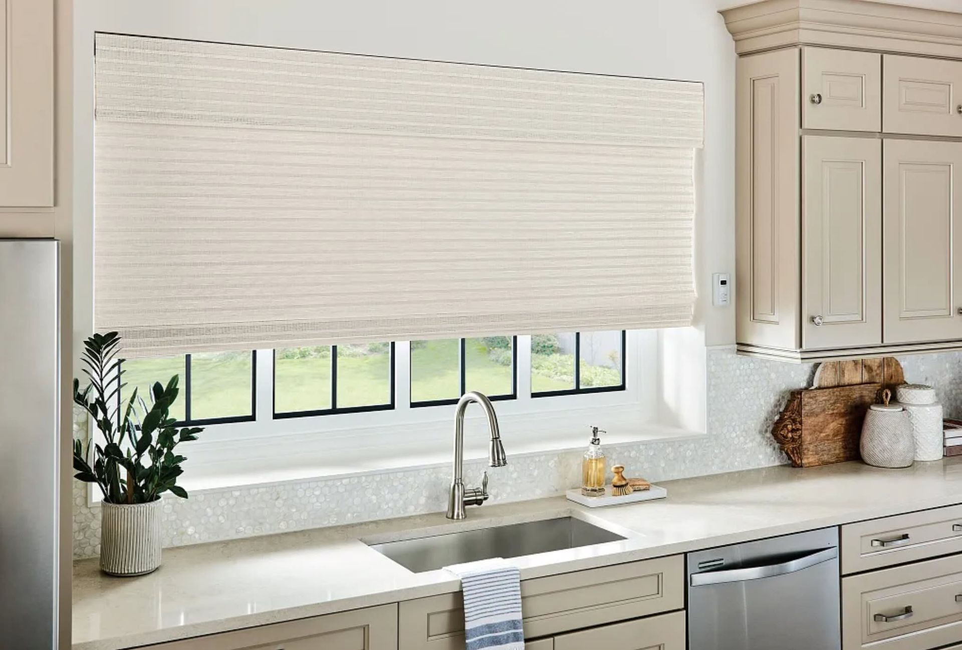 Bright kitchen with large window, white pleated blind, marble countertop, sink, and potted plant.