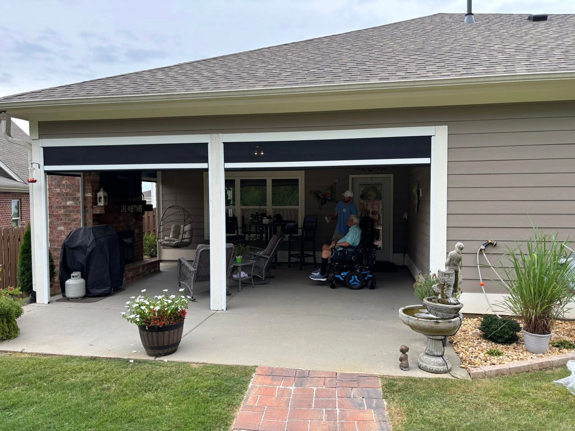 Open garage with patio items, potted flowers, and a person seated inside a suburban home.