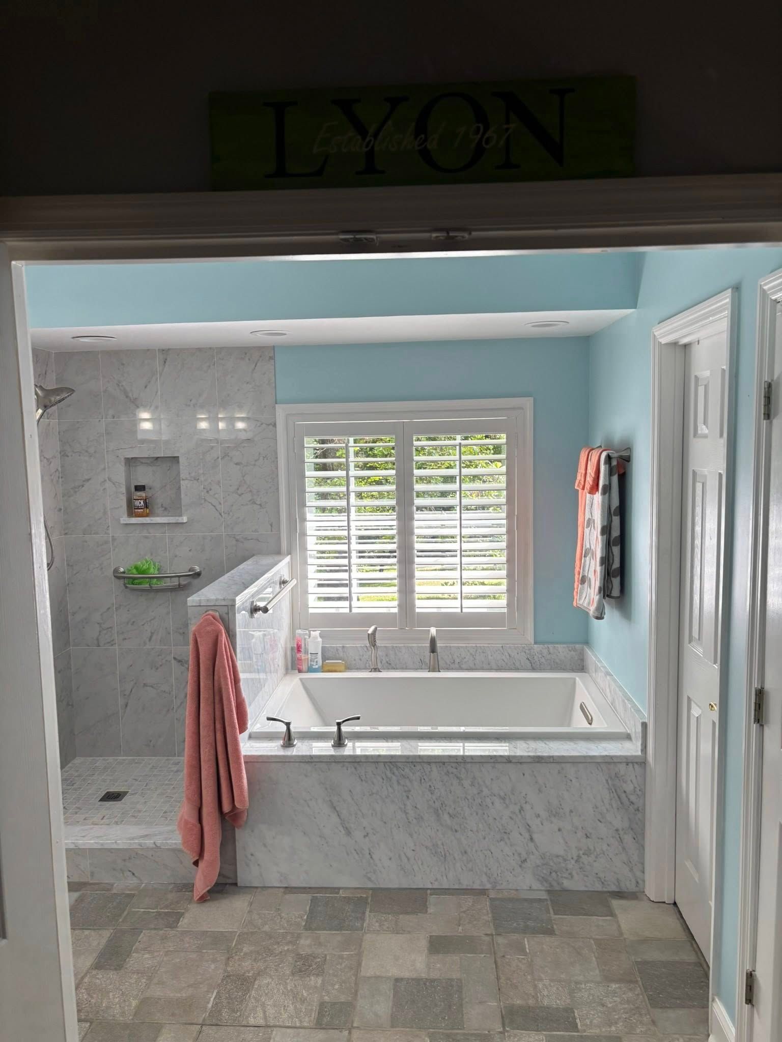 Bright bathroom with marble soaking tub, gray tile floor, blue walls, and a towel hanging nearby.