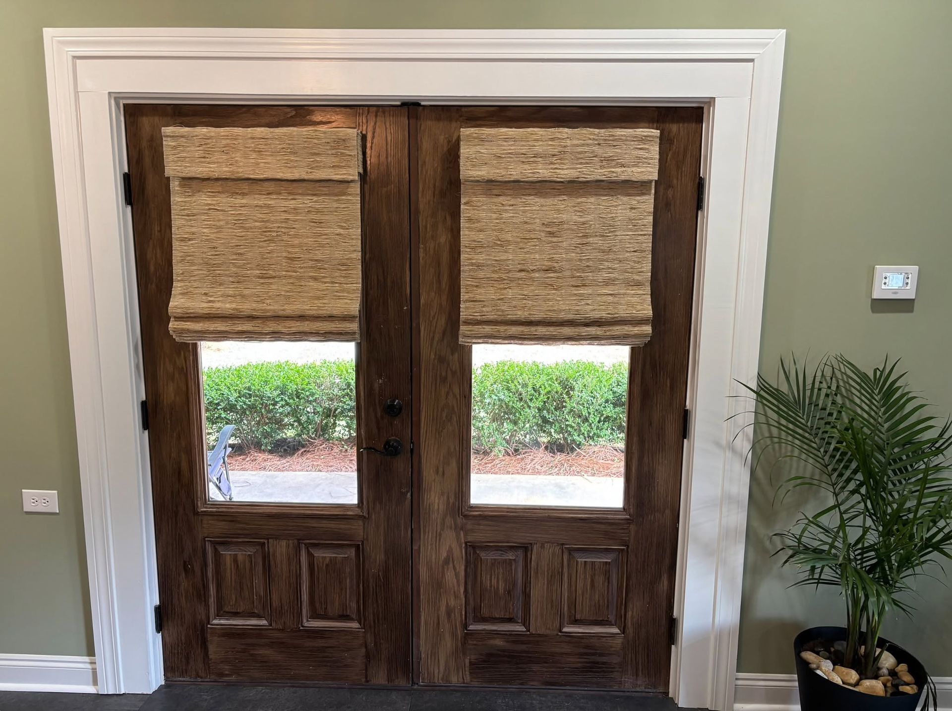 Double wooden French doors with woven shades and small windows in a beige entryway