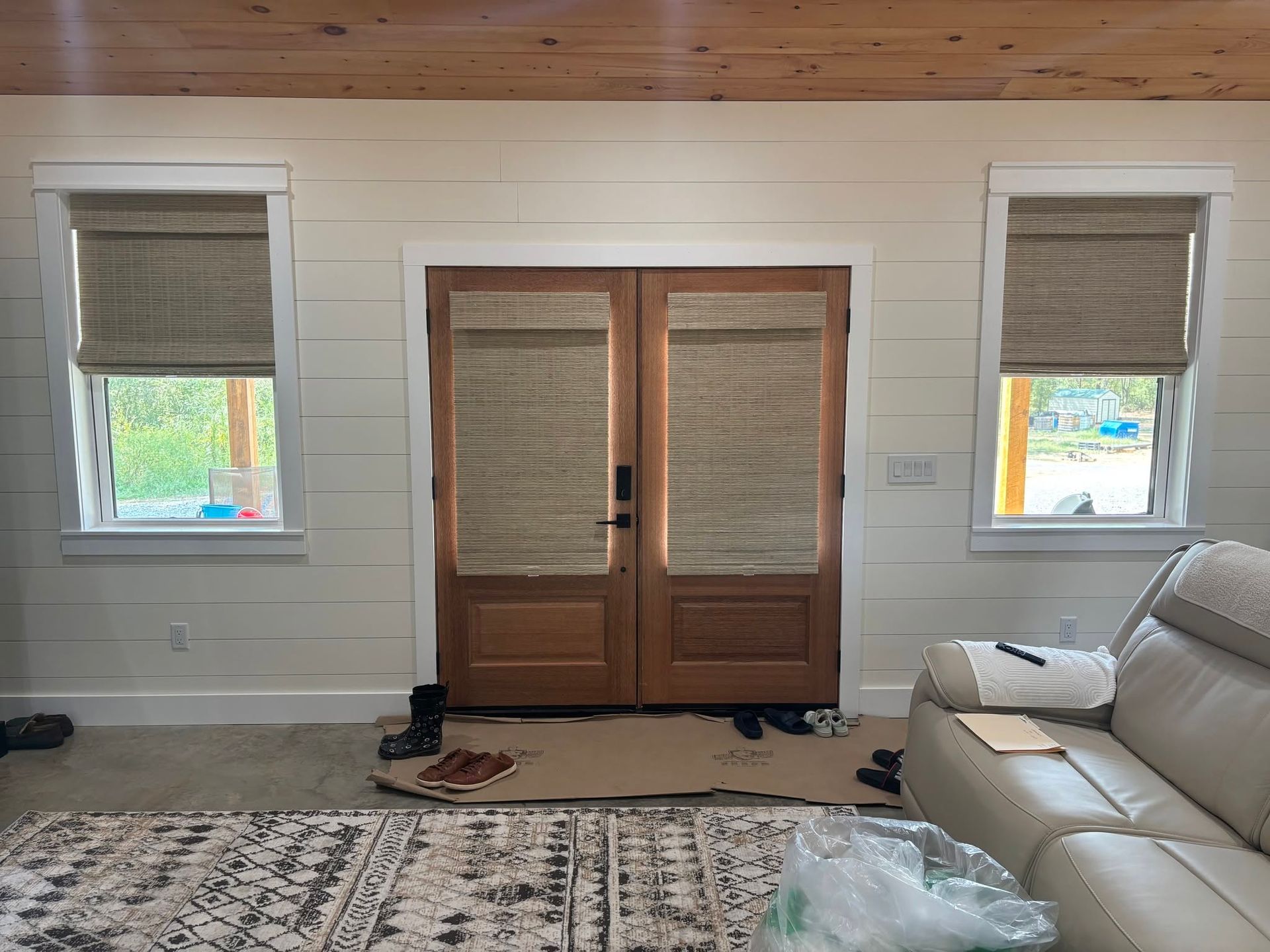 Bright living room with French doors, woven shades, a white sofa, and a patterned rug on hardwood floors.