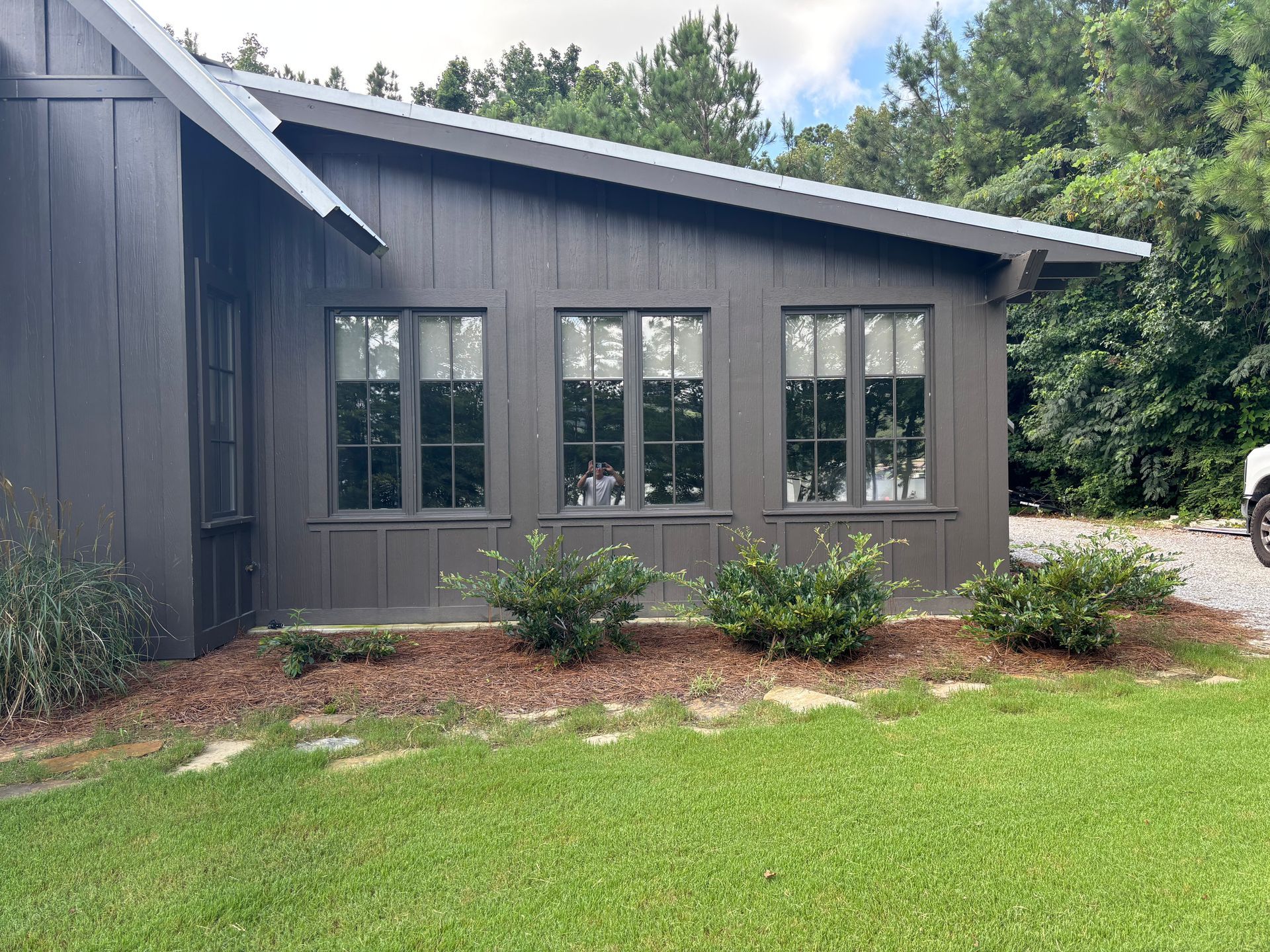 Dark gray house exterior with large windows, sloped roof, and green lawn in front