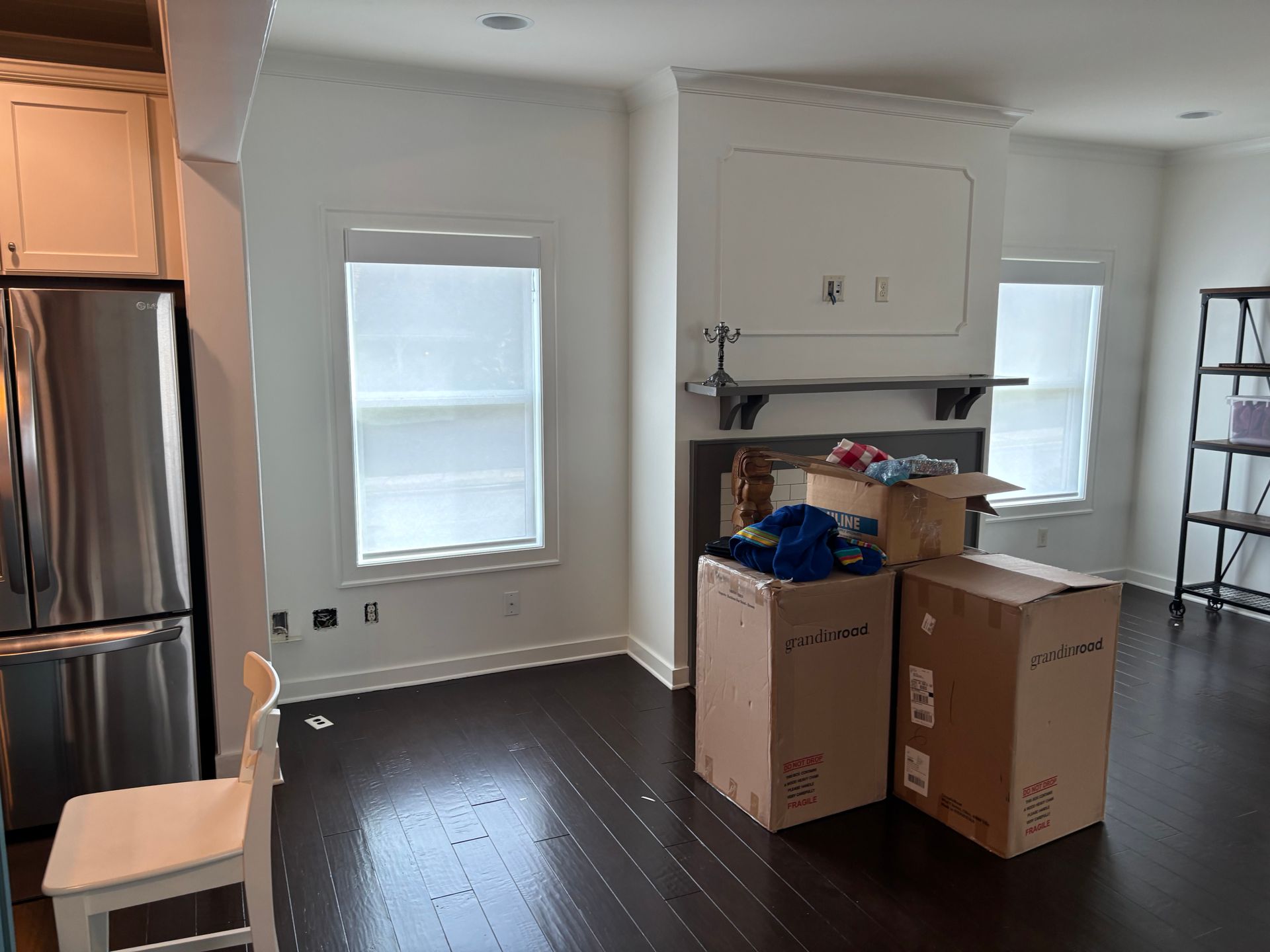 Unfinished kitchen with stainless fridge, dark wood floors, and moving boxes near a shelf and window.