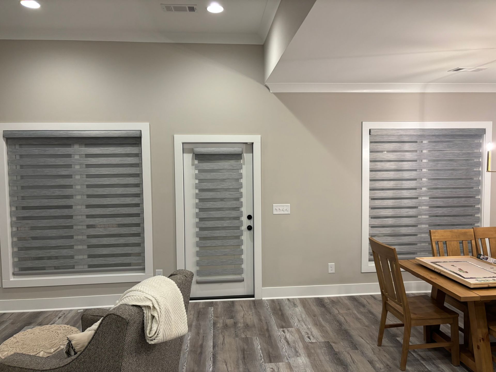 Modern living/dining room with gray walls, wood floors, couch, dining table, and window blinds