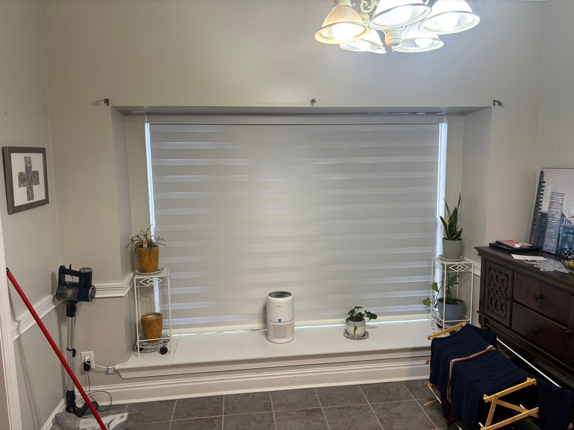 Living room with large window blinds, a floor lamp, plants, and a dresser