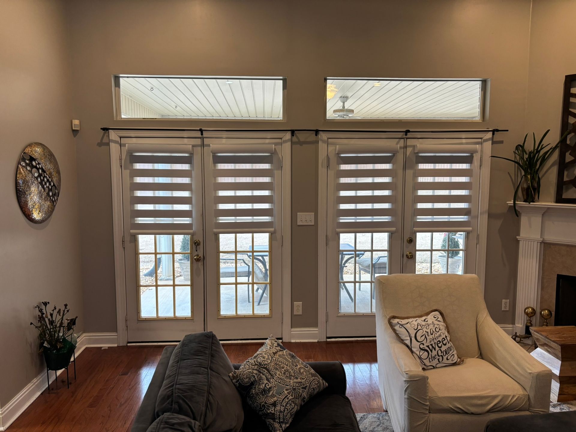 Living room with tall windows, striped shutters, dark sofa, cream chair, and fireplace
