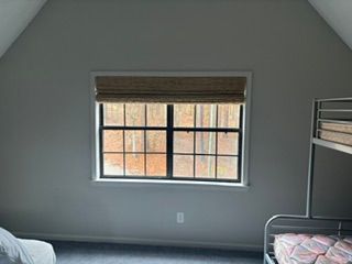 Empty gray attic bedroom with a window, blinds, and a bunk bed on the right.