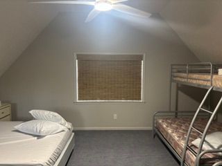 Dorm room with two beds, a bunk bed, and a window with blinds under a ceiling fan.