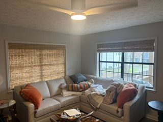 Cozy living room with sectional sofa, orange and patterned pillows, woven shades, and large window.