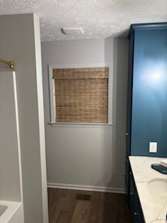 Small bathroom corner with blue vanity, woven window shade, white walls, and dark wood floor.