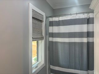 Bathroom corner with a window, gray striped shower curtain, and a woven window shade