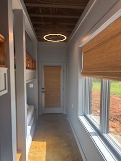 Narrow hallway with bunk beds, large windows, wooden blinds, and a door at the end