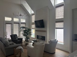 Bright living room with vaulted ceiling, fireplace, TV, and gray and white seating by large windows