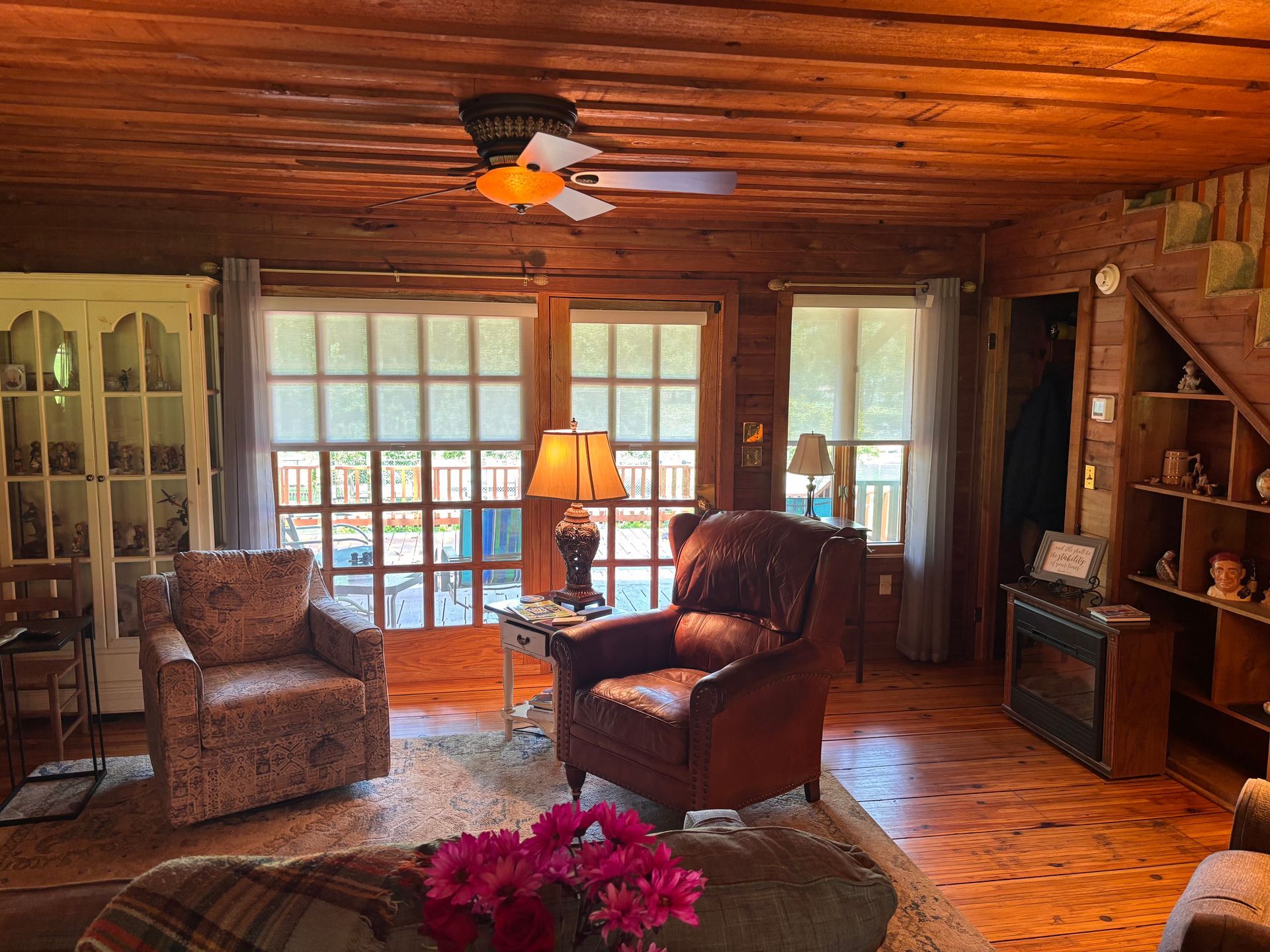 Rustic living room with wood walls, armchairs, lamp, fireplace, and French doors to a deck