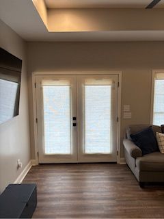 Living room with French doors, gray sofa, wall-mounted TV, and wood flooring