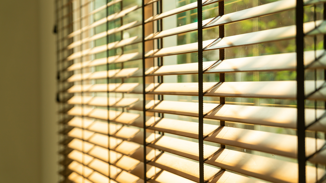 Sunlight streaming through beige window blinds, casting warm stripes across a window