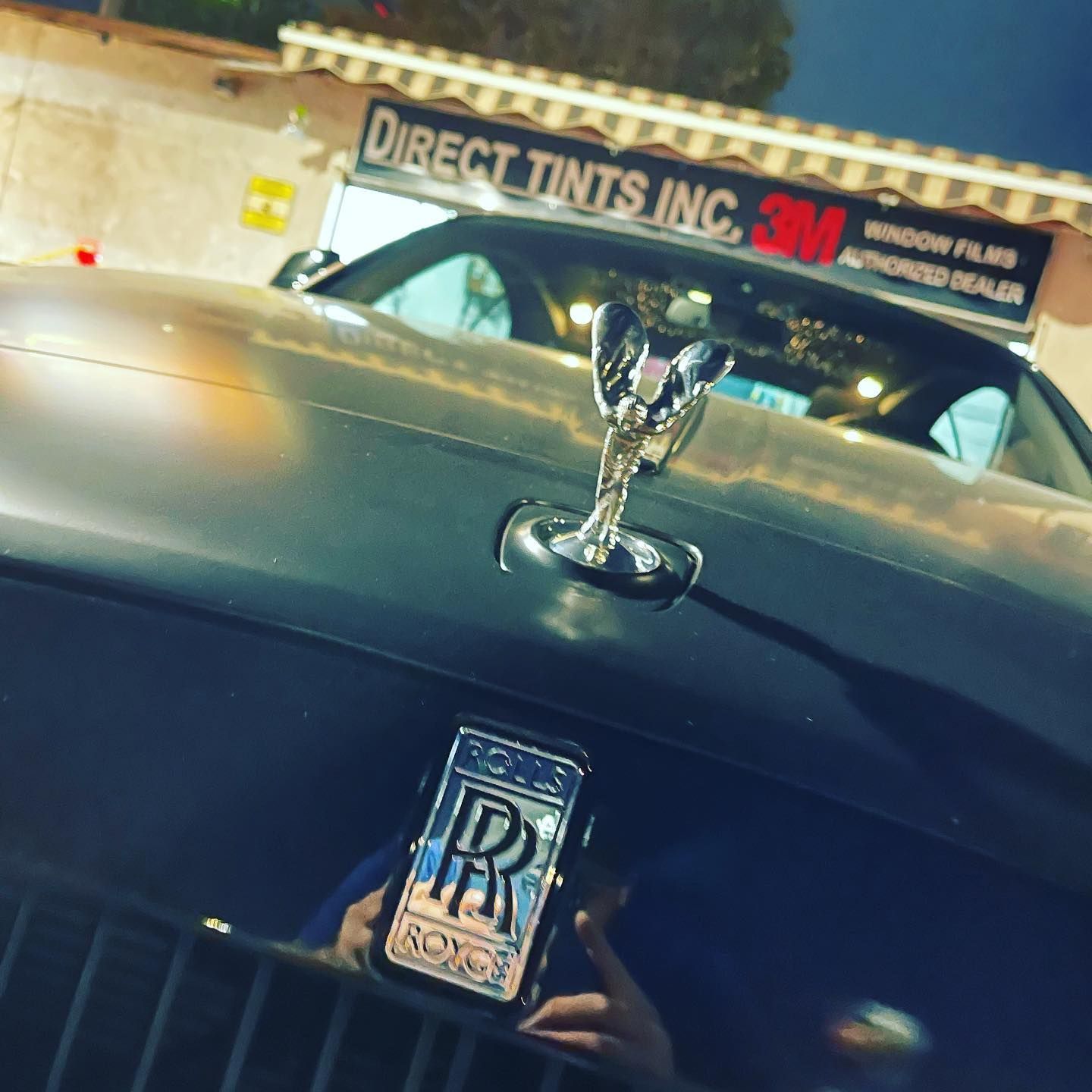 A Rolls-Royce car with a silver hood and Direct Tints Inc. sign in the background.