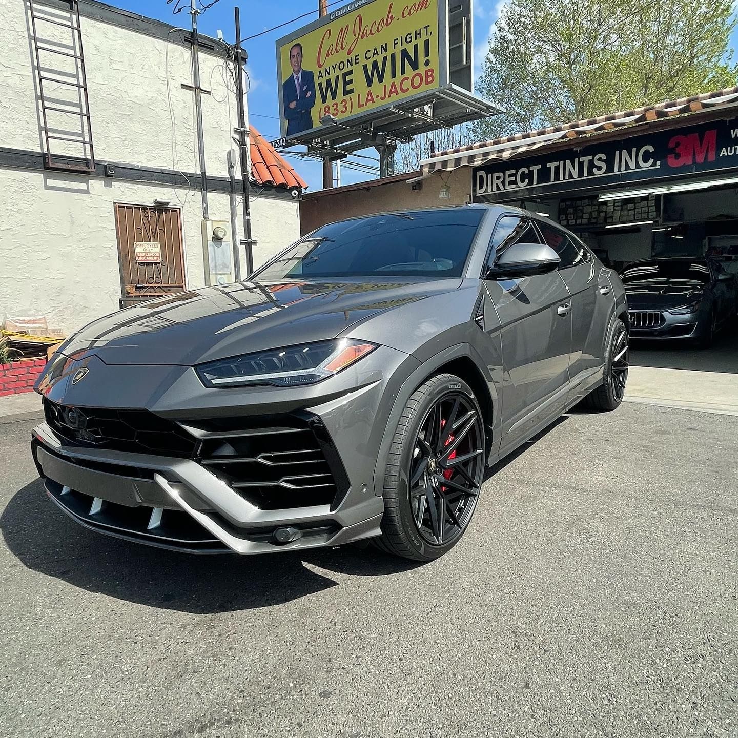 Gray Lamborghini Urus parked in front of a storefront with tinted windows.