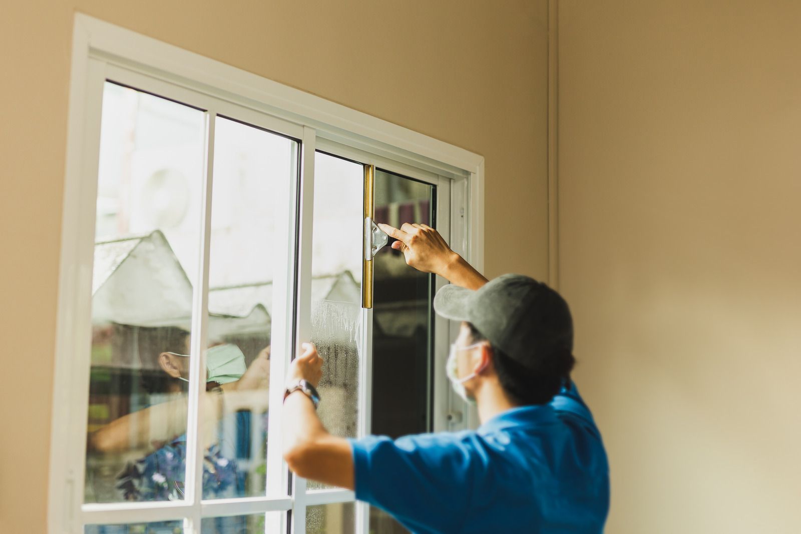 Person installing window film on a white framed window in a room with beige walls.