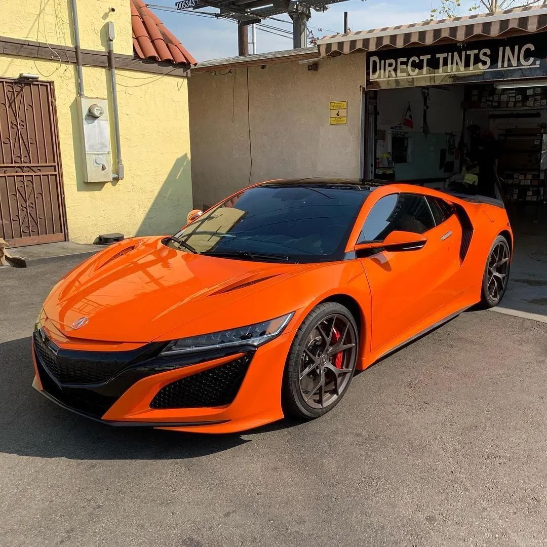 Orange sports car parked outside a tint shop on a sunny day