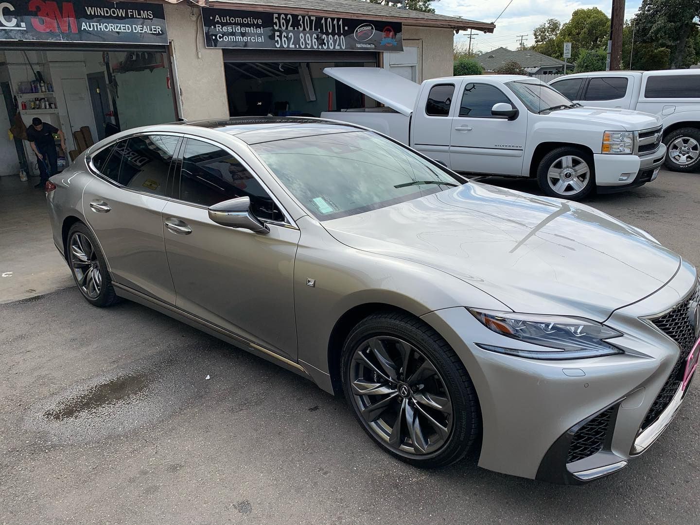 Silver Lexus sedan parked outside a car repair shop; trucks in background.