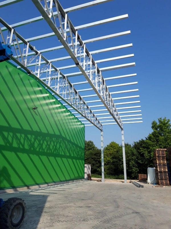 Struttura in acciaio in costruzione accanto a un grande pannello verde a parete in una giornata di sole.