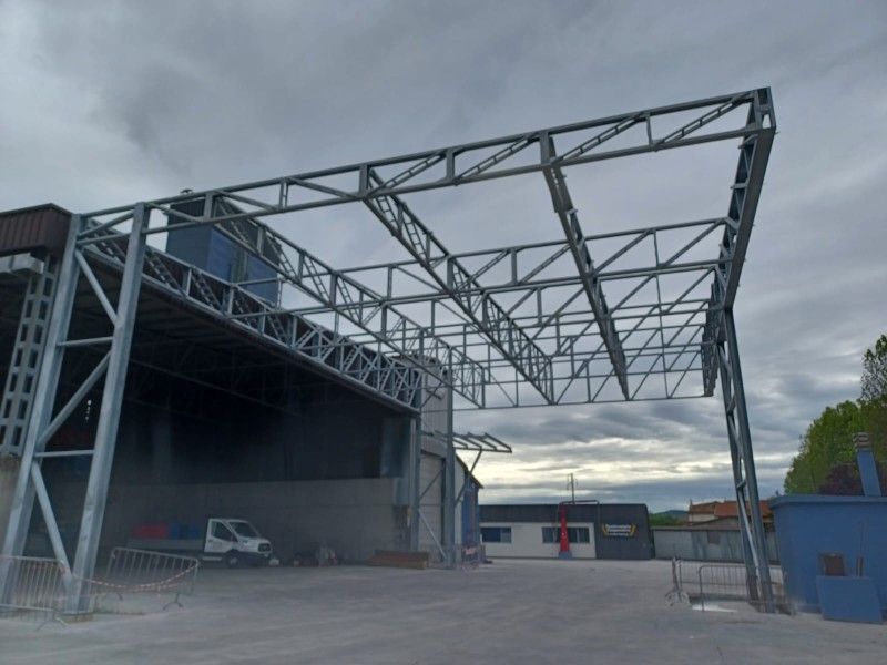 Magazzino industriale con una grande tettoia in acciaio in fase di costruzione in un piazzale aperto.