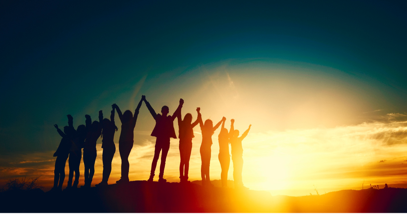 A group of people standing next to each other holding hands at sunset.