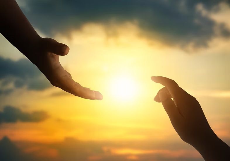Two hands reaching out towards the sun at sunset.