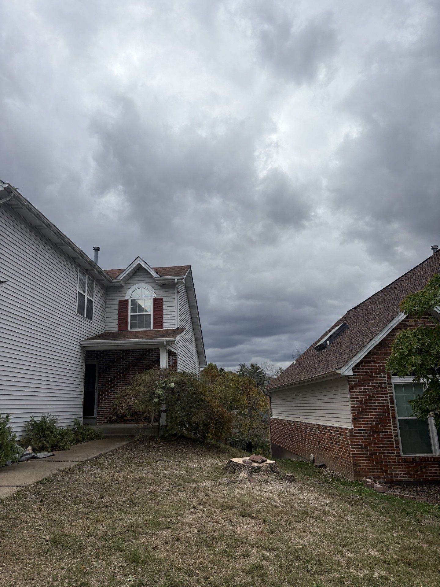 Two-story house with red roof under cloudy sky, adjacent to a brick house. Overcast day.